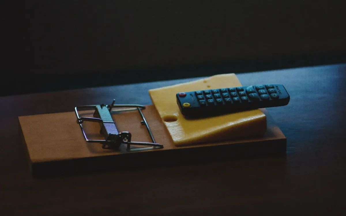 Une télécommande télé posée sur du fromage dans une souricière, illustrant le piège dissimulé derrière l'IPTV gratuit au Canada